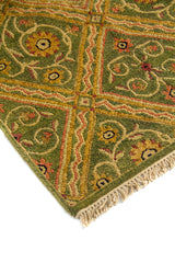 Acercamiento de alfombra artesanal con patrón de rombos entrelazados, flores estilizadas y combinación de verde, beige y rojo.