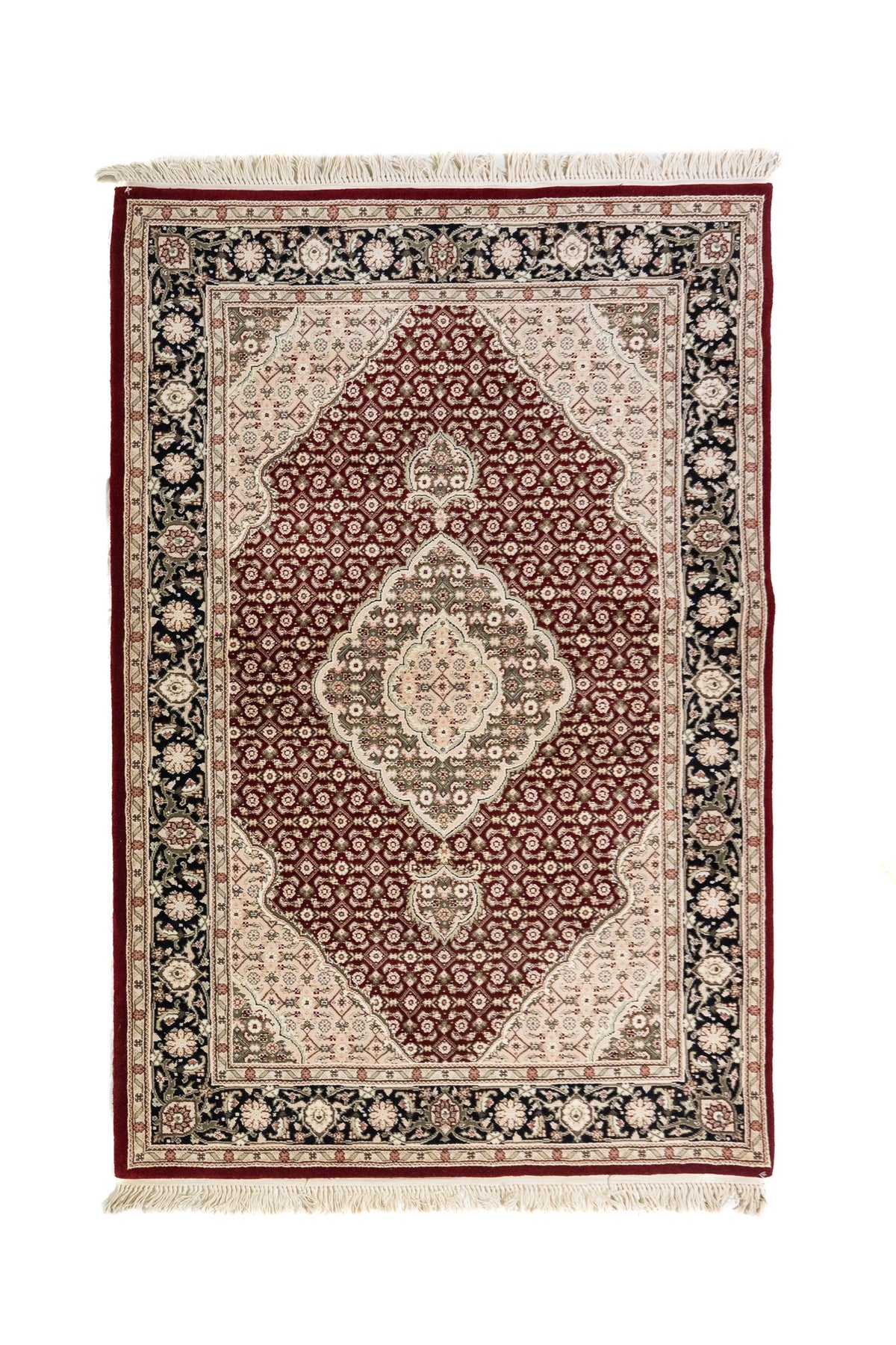 Alfombra clásica en tono rojo con medallón central blanco suave y gris, fondo de pequeños motivos geométricos y guarda floral negra con flecos.