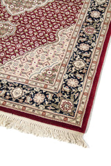 Acercamiento de alfombra clásica con patrón repetitivo en fondo rojo oscuro, borde floral oscuro y detalles ornamentales en blanco suave y tonos suaves.