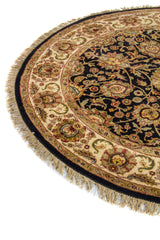 Primer plano de alfombra circular clásica con borde floral en tonos beige y dorado sobre fondo oscuro.