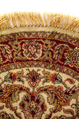 Detalle de alfombra redonda con guarda roja, fondo beige y motivos ornamentales florales.