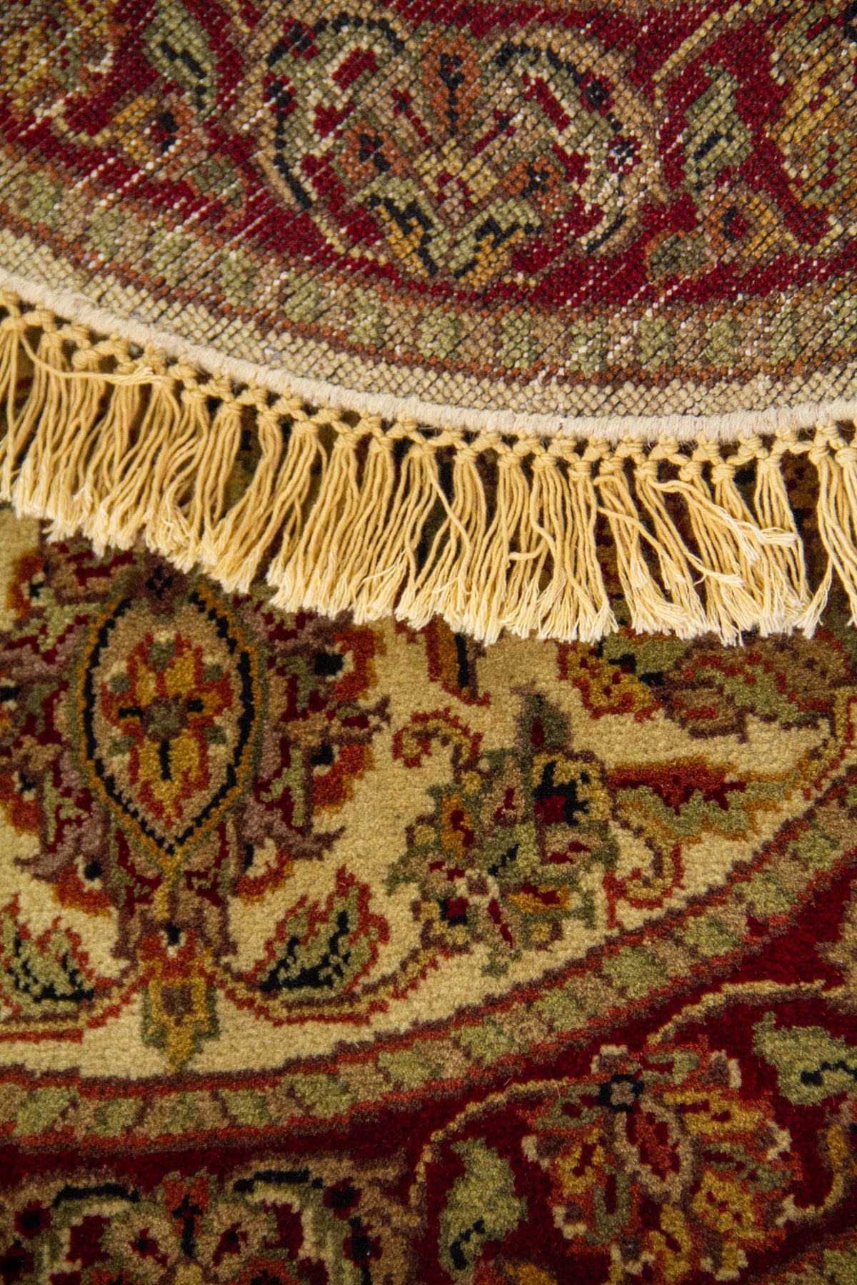 Detalle de alfombra redonda doblada con diseño floral clásico, borde decorativo y flecos artesanales.