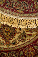 Detalle de alfombra redonda doblada con diseño floral clásico, borde decorativo y flecos artesanales.