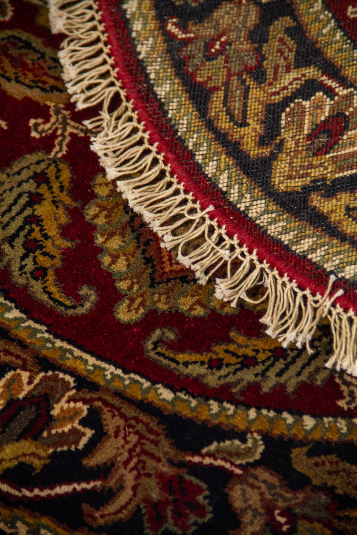 Detalle de alfombra redonda doblada con diseño ornamental clásico, borde oscuro y flecos decorativos.