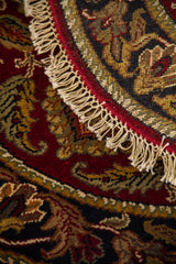 Detalle de alfombra redonda doblada con diseño ornamental clásico, borde oscuro y flecos decorativos.