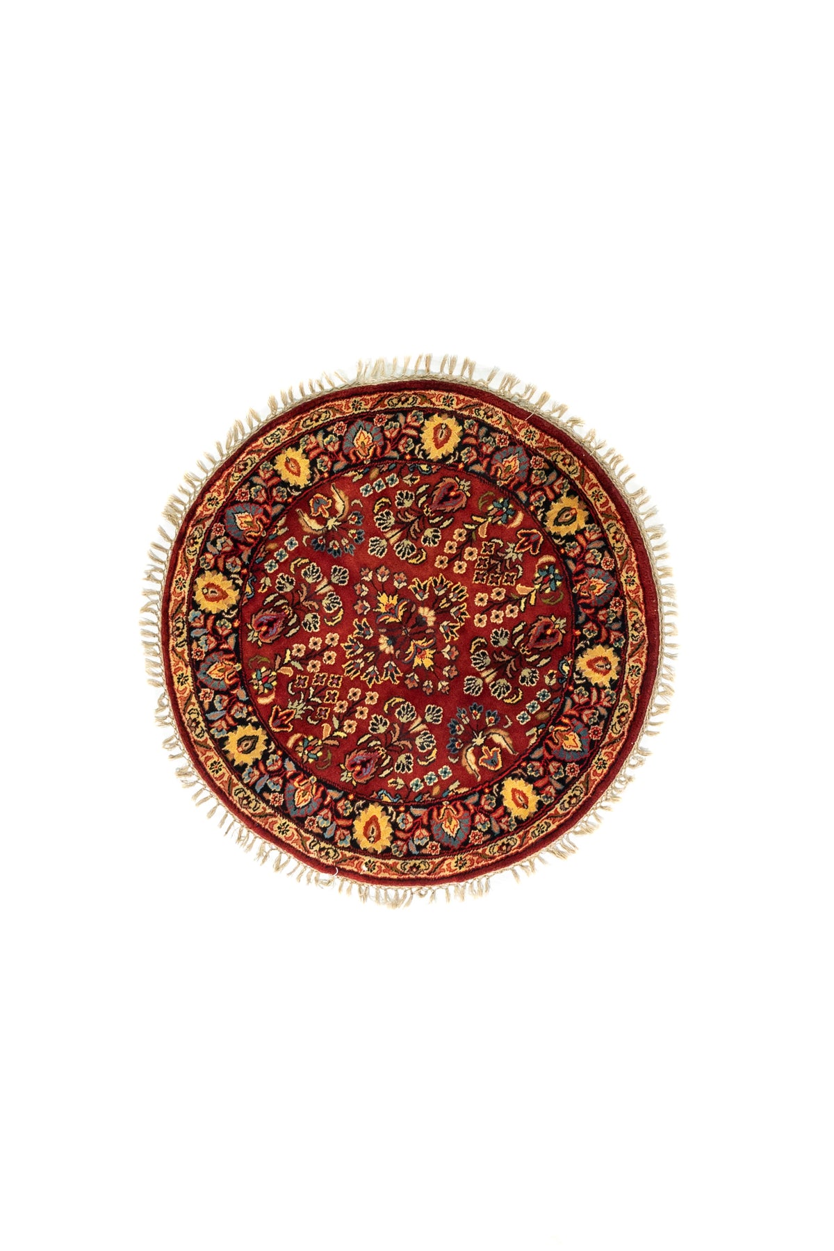 Alfombra redonda de estilo oriental en tonos rojo, azul oscuro y beige con motivos florales y flecos decorativos.