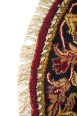 Primer plano del borde de alfombra redonda con guarda azul oscuro, detalles florales y flecos decorativos.