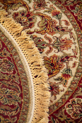 Detalle de alfombra redonda con diseño floral en tonos beige y rojo, borde decorativo y flecos.