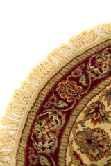 Primer plano del borde de alfombra redonda con guarda roja, detalles ornamentales y flecos en tono beige.