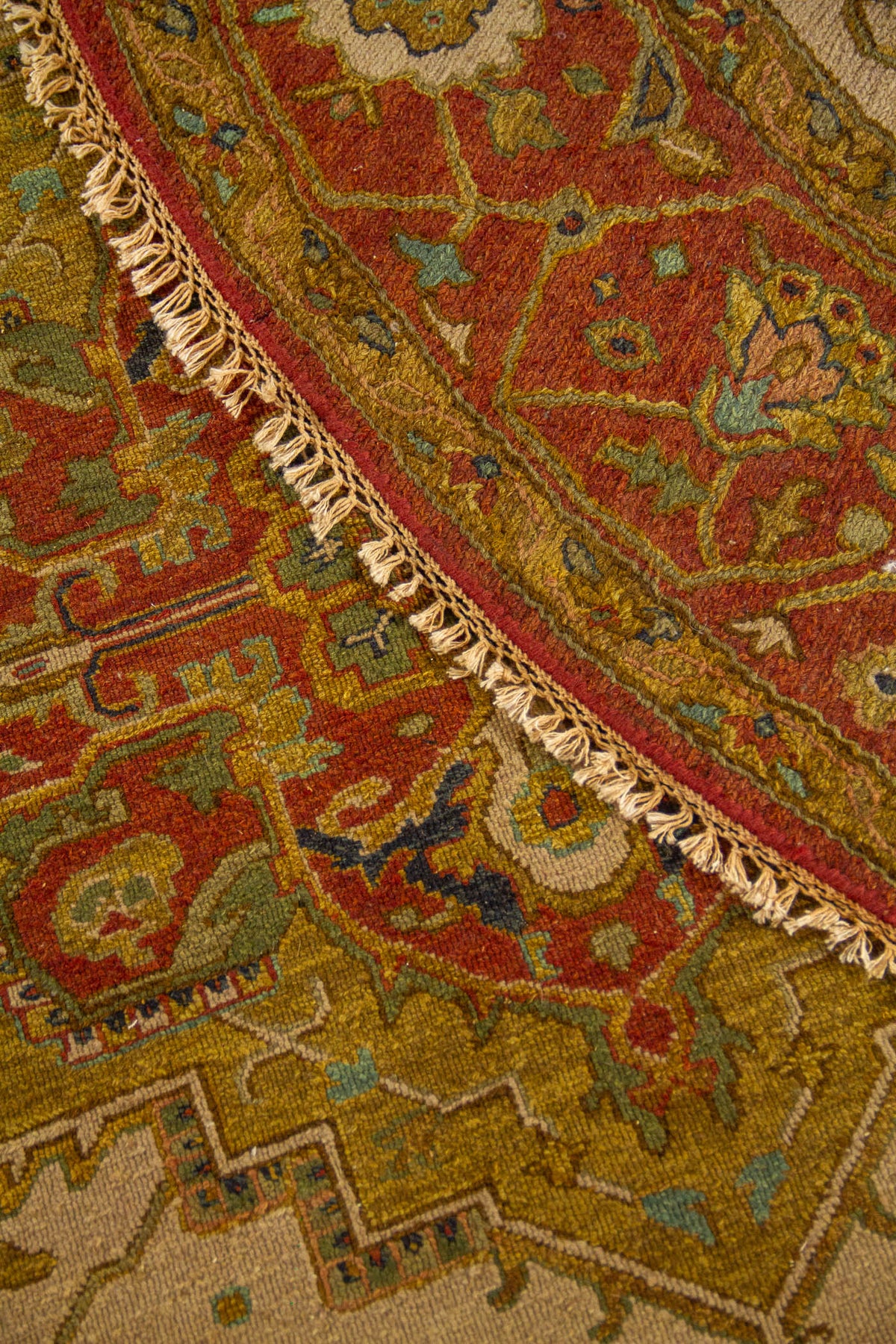 Acercamiento de la alfombra doblada mostrando la textura del tejido, la guarda ornamental y los flecos laterales.