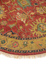 Detalle de alfombra redonda con diseño floral y geométrico en tonos rojo, verde oliva y dorado.