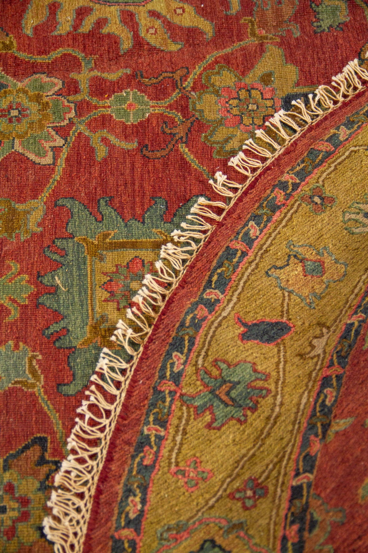 Alfombra redonda doblada con detalle de guarda decorativa, fondo rojizo y flecos artesanales.
