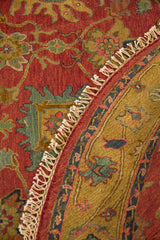 Alfombra redonda doblada con detalle de guarda decorativa, fondo rojizo y flecos artesanales.