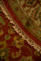 Detalle de alfombra redonda doblada con textura tejida, guarda ornamental y flecos artesanales.