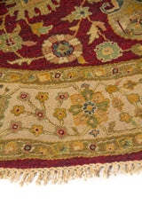 Detalle de alfombra redonda con fondo rojo, guarda beige y delicados motivos florales tejidos.