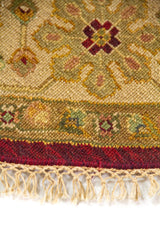 Primer plano del borde de alfombra redonda con diseño ornamental en tonos beige, amarillo y rojo.
