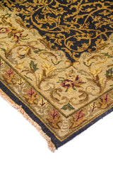 Detalle de esquina de alfombra elegante con fondo azul oscuro, arabescos dorados y marco floral en tonos beige y verde oscuro