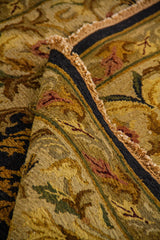 Detalle de alfombra doblada mostrando textura del tejido, reverso y diseño floral decorativo en tonos beige, dorado y azul oscuro