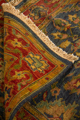 Detalle de alfombra doblada mostrando textura del tejido, reverso y diseño floral clásico en tonos azul, rojo y beige