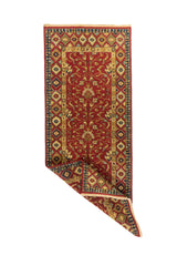 Alfombra pasillera roja con esquina doblada que muestra el reverso del tejido y el detalle de la guarda decorativa