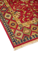 Primer plano lateral de alfombra tradicional con fondo rojo intenso, diseño floral simétrico y guarda de figuras geométricas