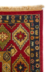 Detalle de flecos y esquina de alfombra oriental con rombos decorativos, borde azul oscuro y fondo rojo vibrante