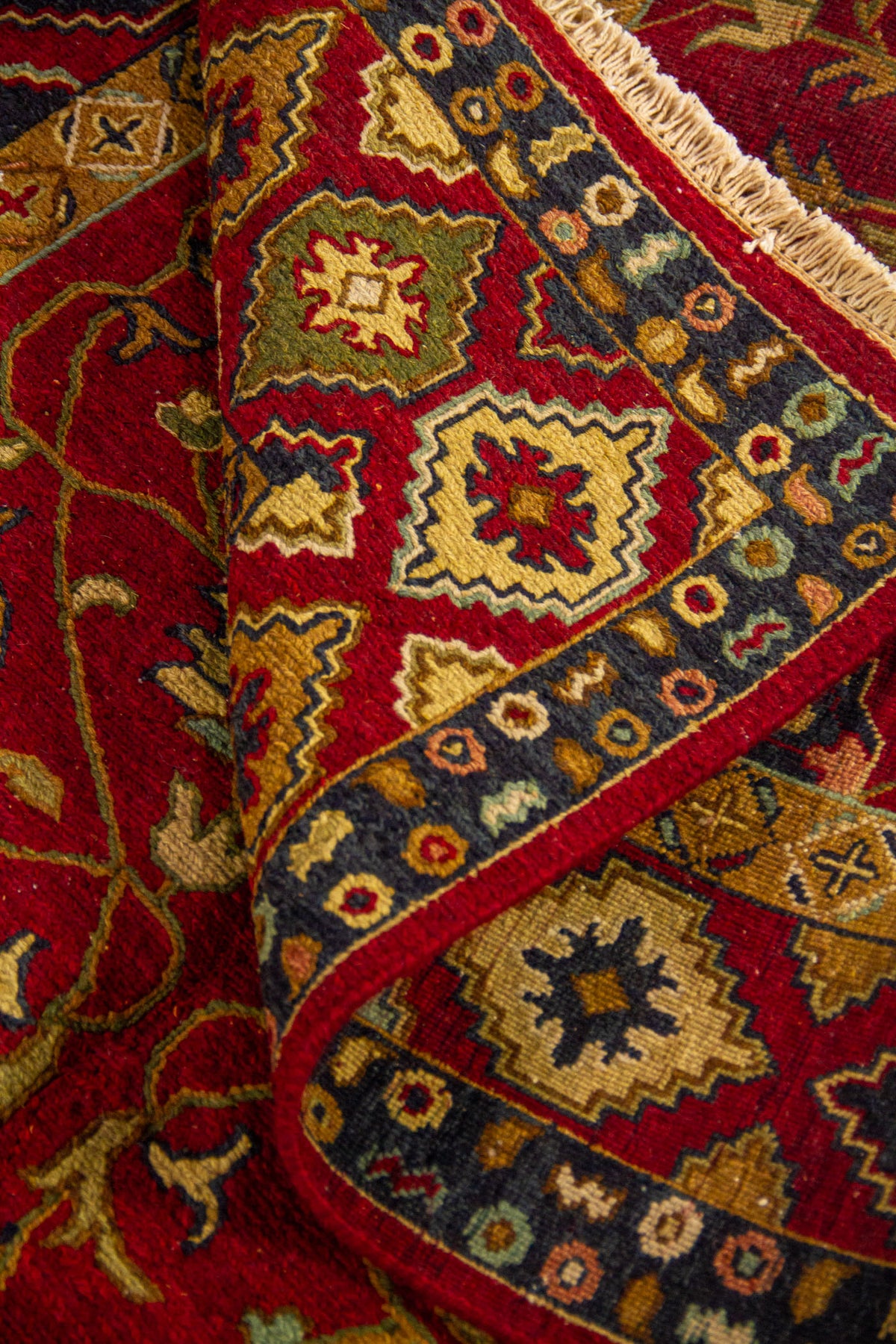 Detalle de alfombra doblada mostrando textura, grosor y combinación de motivos florales y geométricos en tonos cálidos
