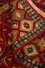 Detalle de alfombra doblada mostrando textura, grosor y combinación de motivos florales y geométricos en tonos cálidos