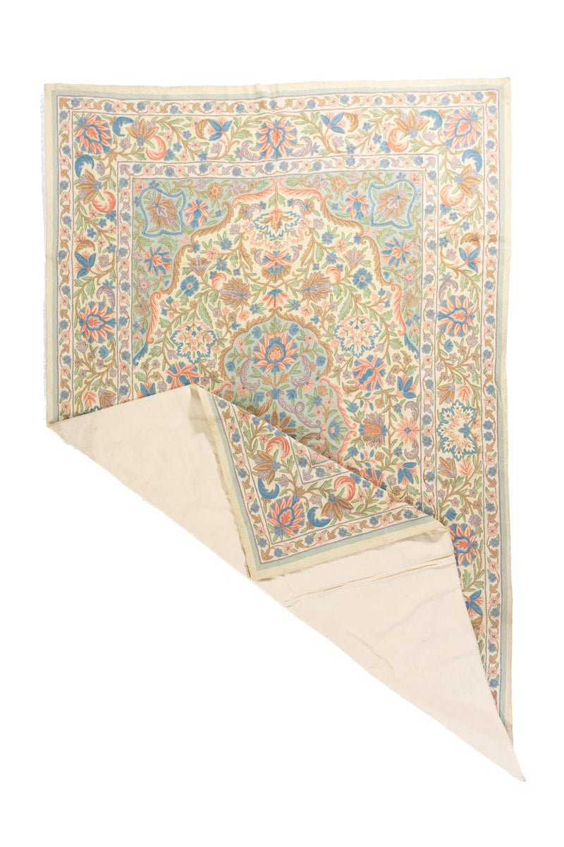 La alfombra aparece con una esquina levantada, permitiendo apreciar su caída, flexibilidad y el reverso claro del tejido. Esta imagen resalta tanto su acabado como la continuidad del diseño floral en toda la superficie.