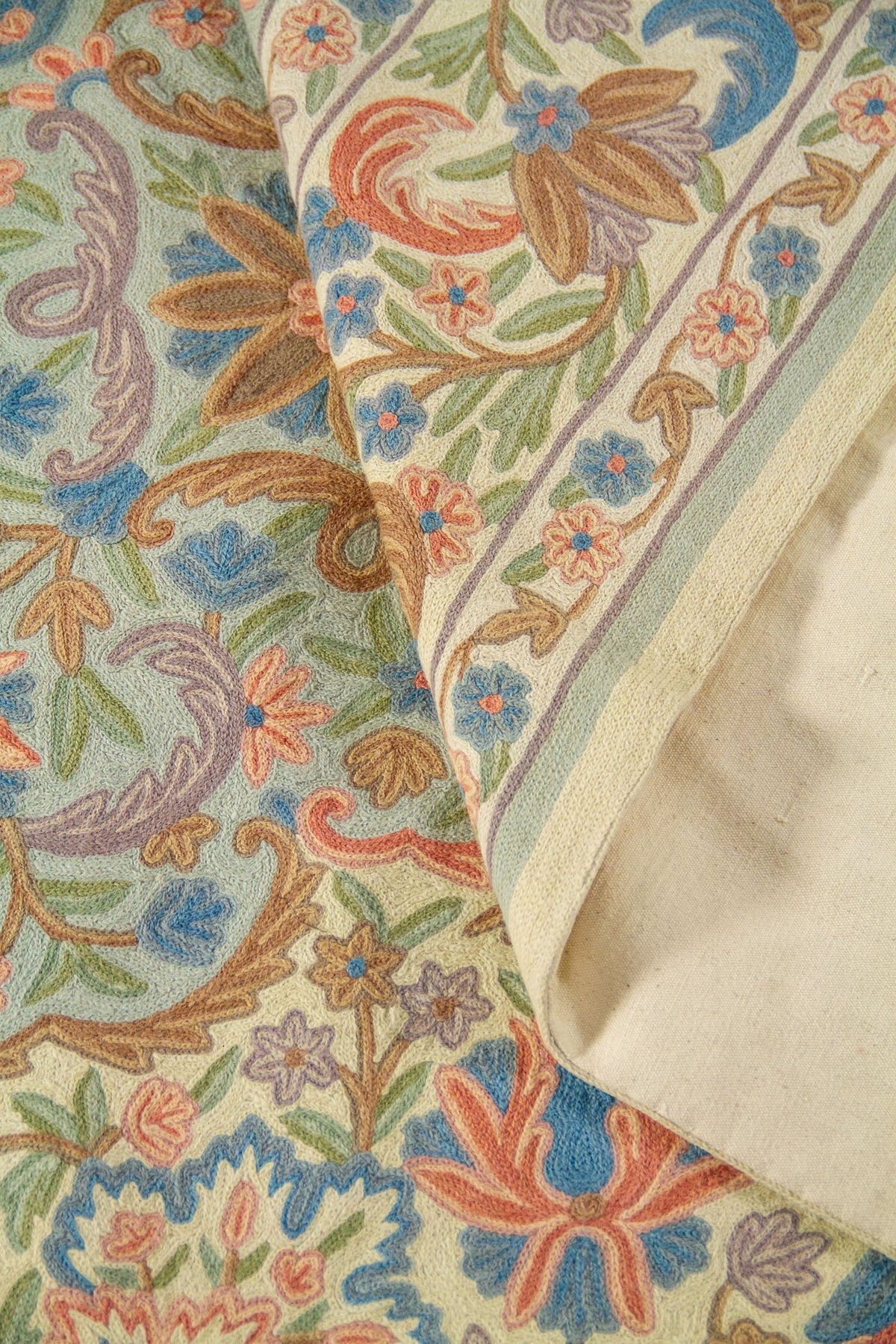 La alfombra se muestra parcialmente doblada para destacar su textura, flexibilidad y estructura. El acercamiento permite observar mejor la densidad del diseño y el cuidado en la ejecución de cada motivo floral.