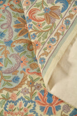 La alfombra se muestra parcialmente doblada para destacar su textura, flexibilidad y estructura. El acercamiento permite observar mejor la densidad del diseño y el cuidado en la ejecución de cada motivo floral.
