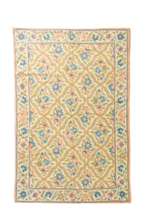 Alfombra de estilo floral en tonos suaves, con fondo blanco suave, flores celestes y anaranjado suave, hojas verdes y un patrón repetitivo enmarcado por una guarda decorativa.
