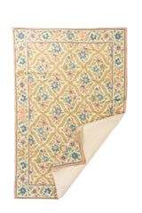 Alfombra floral en tonos pastel con una esquina doblada, mostrando el reverso liso y el diseño de flores azules, rosadas y verdes sobre fondo claro.