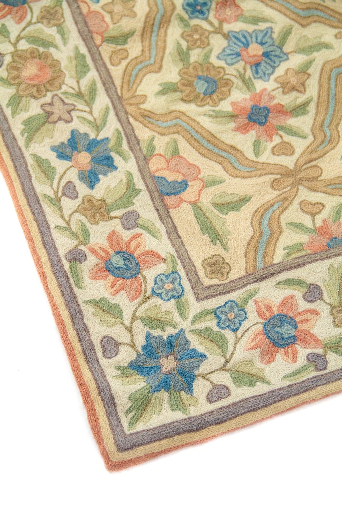 Detalle de esquina de alfombra con guarda floral y patrón interior geométrico curvilíneo, en colores blanco suave, celeste, anaranjado suave, verde y beige