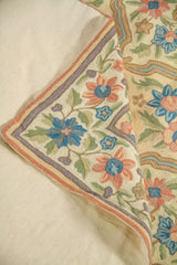 Primer plano de alfombra doblada que deja ver el reverso, destacando las flores bordadas en tonos pastel y los contornos suaves del diseño.