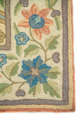 Acercamiento de la guarda floral de la alfombra, con flores azules y anaranjado suave, hojas verdes y líneas decorativas en tonos morado y beige.