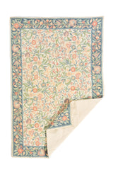 Alfombra floral rectangular con esquina doblada mostrando el reverso en tono beige claro