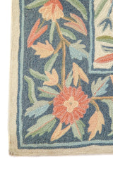 Detalle de esquina de alfombra floral con flor anaranjado suave y hojas en tonos verdes sobre guarda azul