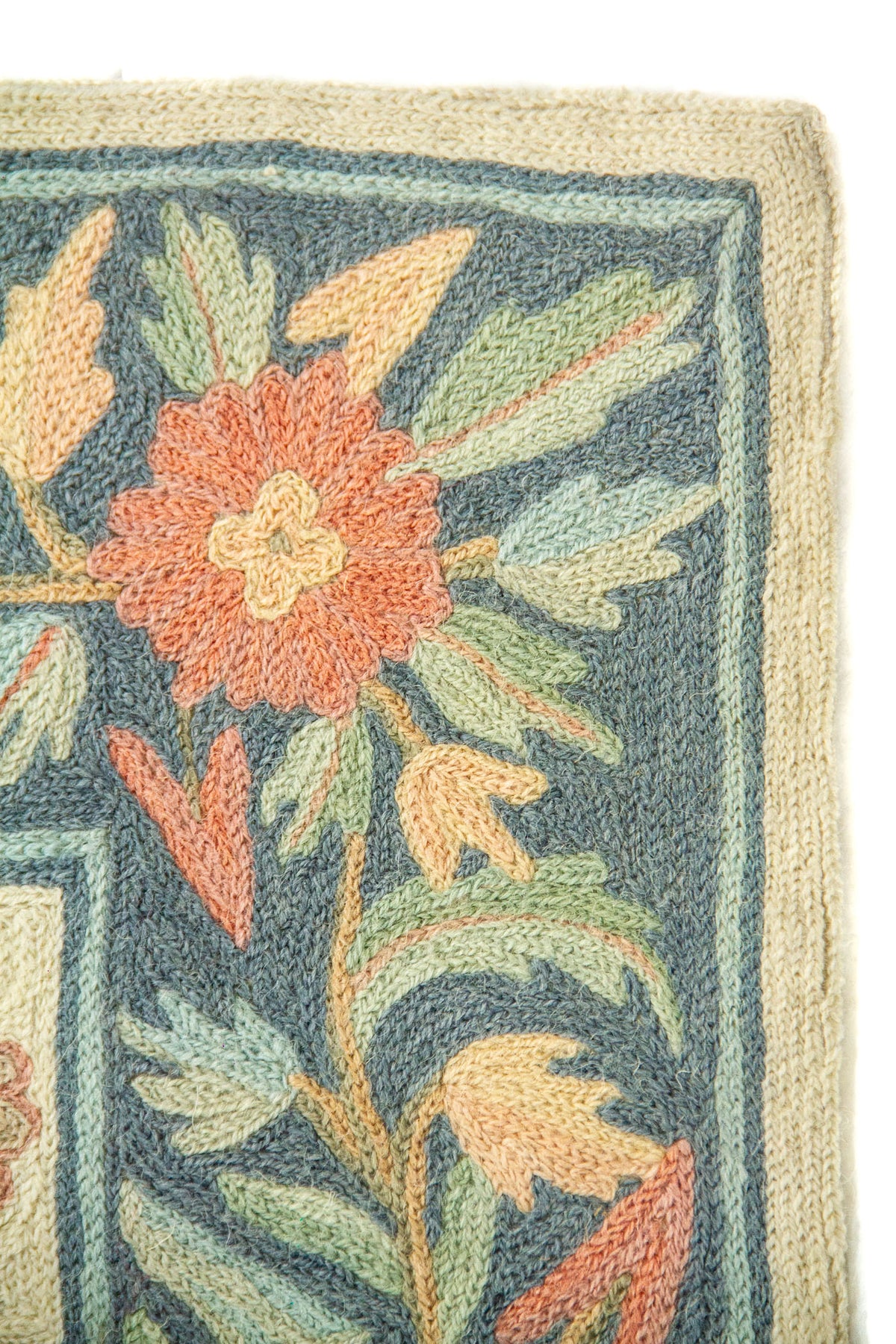 Primer plano de borde de alfombra con diseño botánico en tonos pastel y fondo azul claro