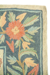 Primer plano de borde de alfombra con diseño botánico en tonos pastel y fondo azul claro