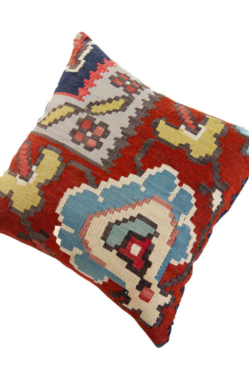Detalle de textura de almohadón kilim con motivos geométricos en celeste y rojo