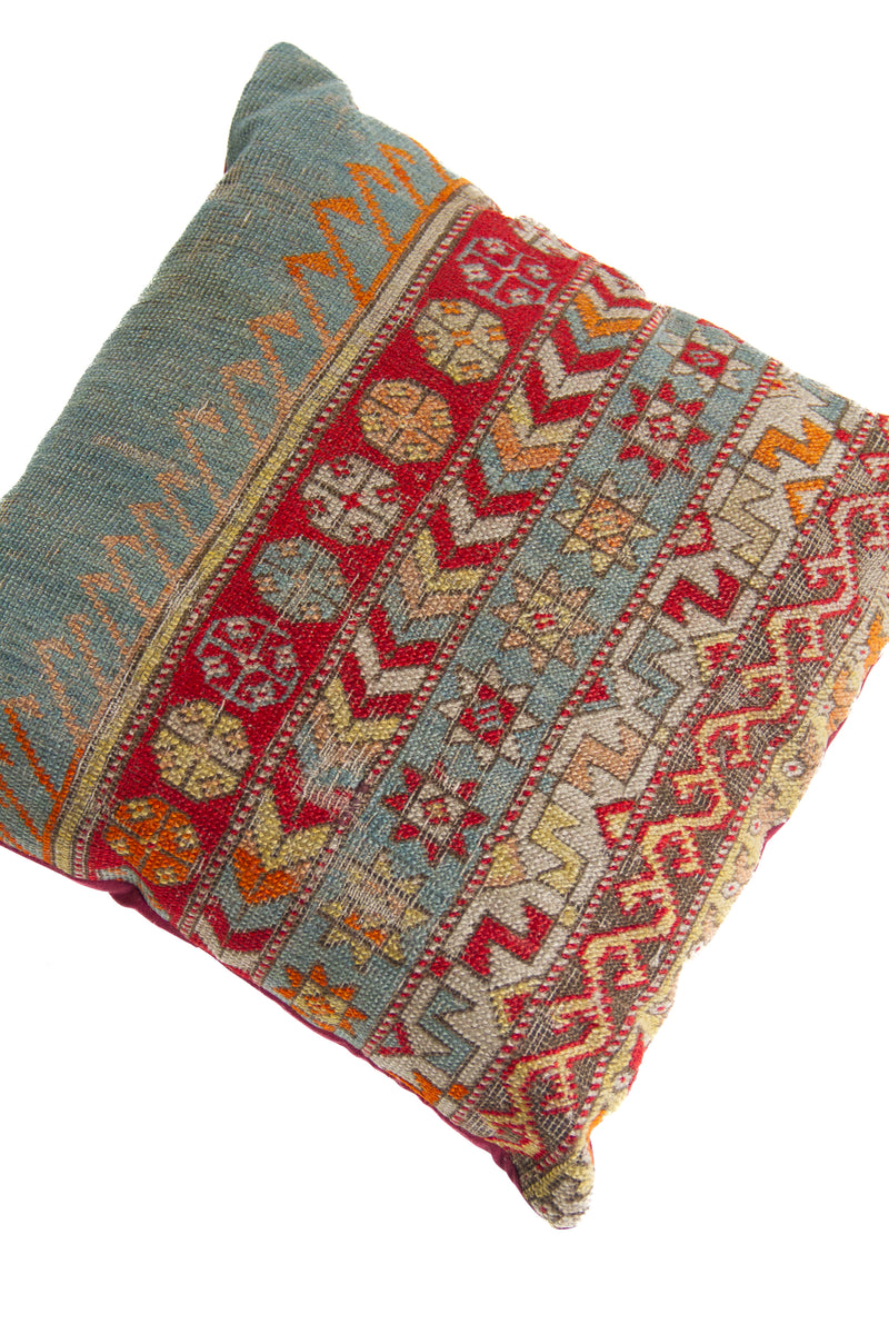 Detalle de textura de almohadón kilim con guardas geométricas, rombos y franjas en celeste y rojo