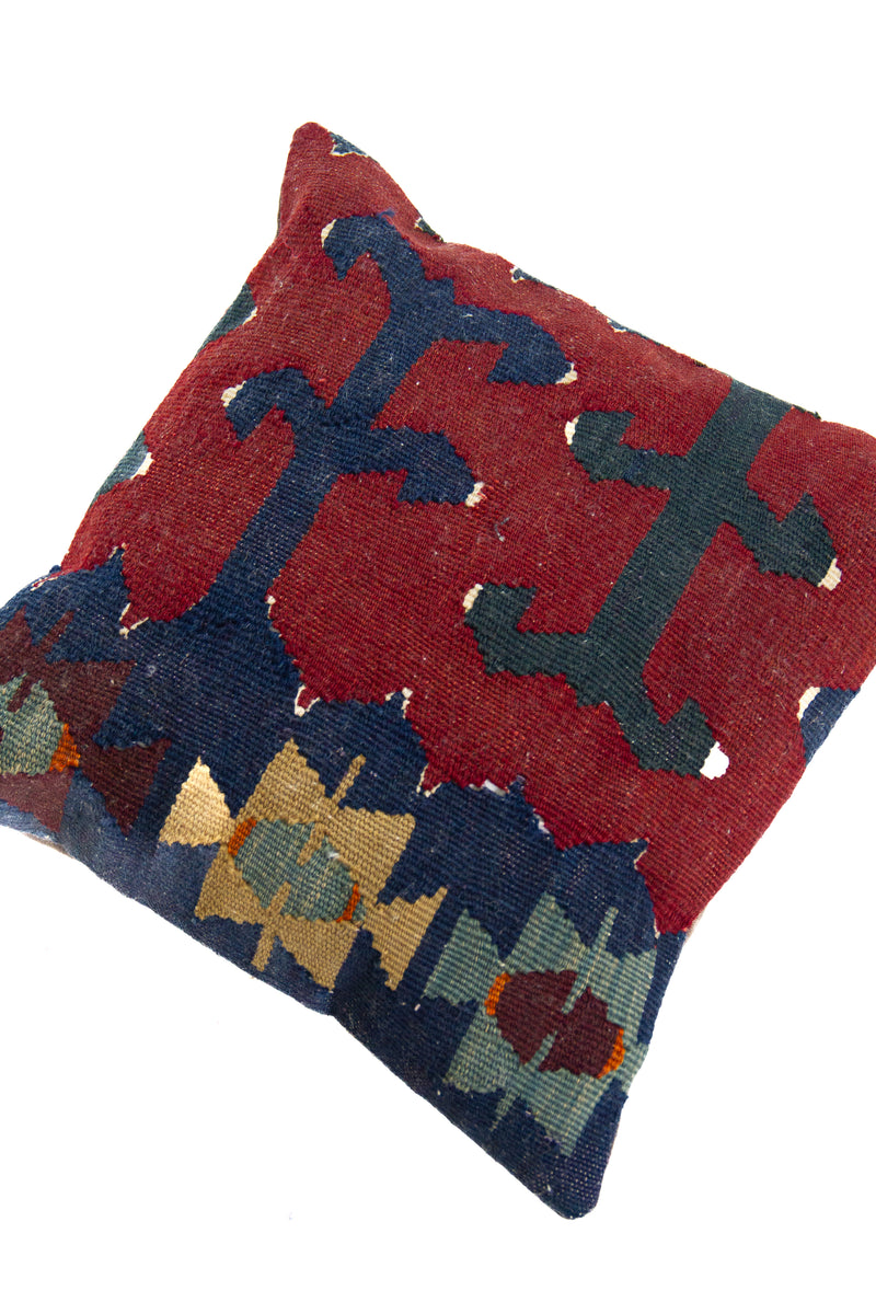 Detalle de textura de almohadón kilim con motivos geométricos en azul oscuro, bordó y verde