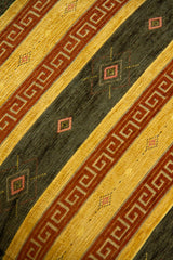 Detalle de textura de almohadón beige con rayas verdes, grecas marrones y rombos decorativos