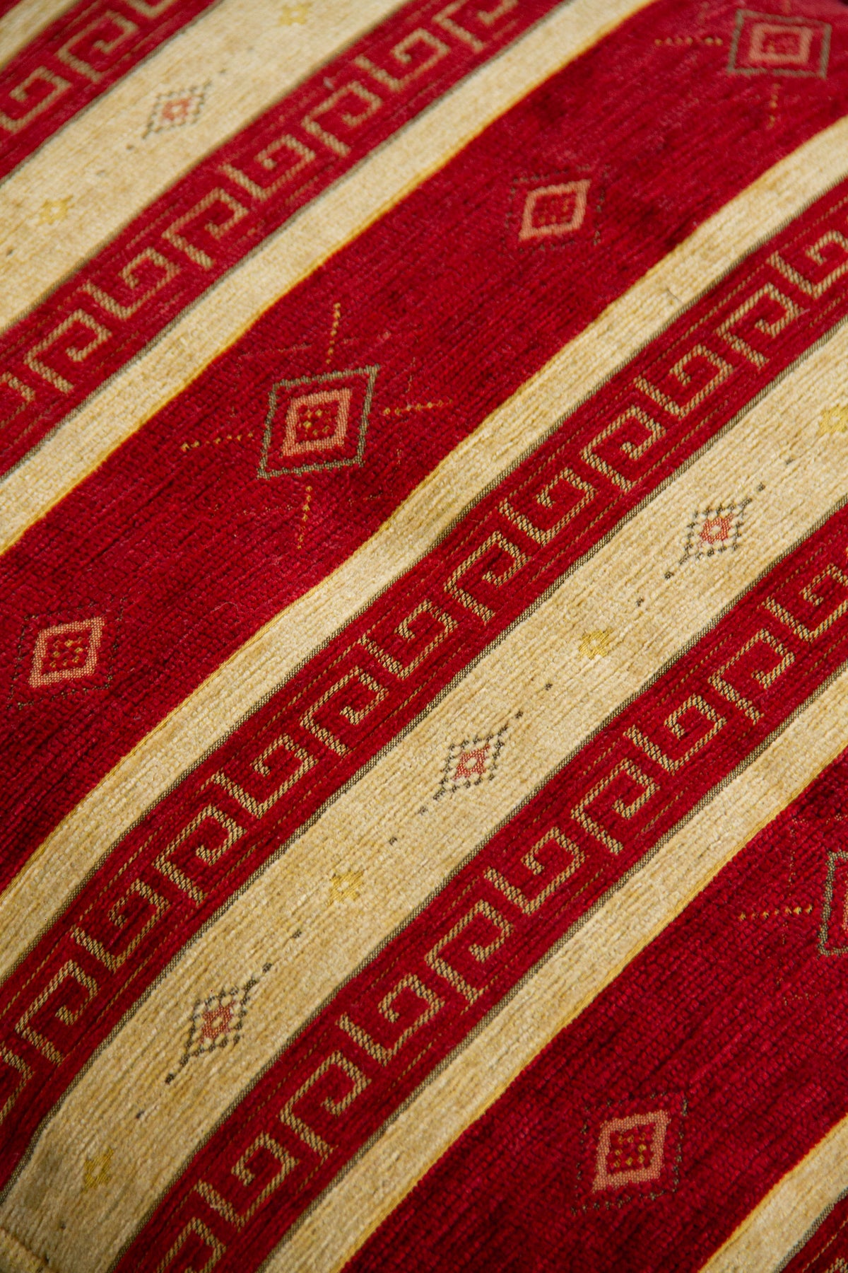 Detalle de textura de almohadón rojo con rayas beige, grecas y rombos decorativos