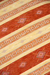 Detalle de textura de almohadón terracota con rayas beige, guardas geométricas y rombos decorativos