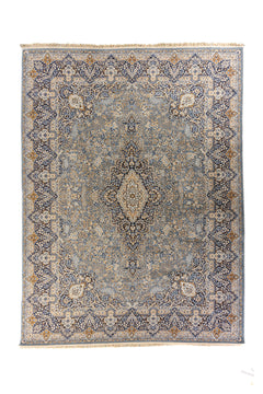 Vista cenital completa de la alfombra con diseño simétrico floral en tonos suaves de gris, azul y dorado.
