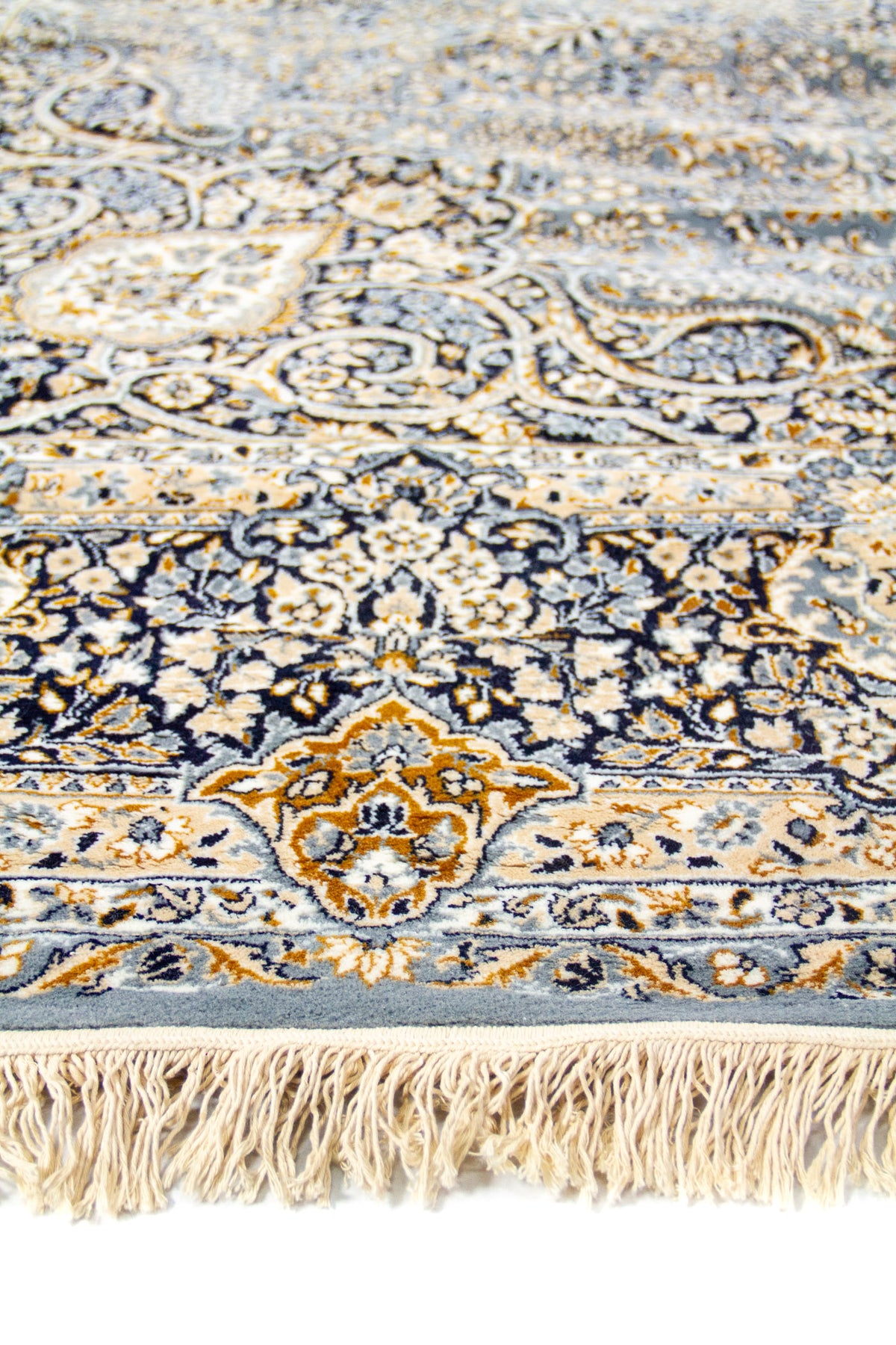 Detalle en primer plano del borde de la alfombra con flecos y patrones florales elaborados en azul y dorado.