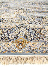 Detalle en primer plano del borde de la alfombra con flecos y patrones florales elaborados en azul y dorado.