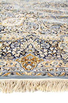 Detalle en primer plano del borde de la alfombra con flecos y patrones florales elaborados en azul y dorado.